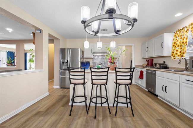 Kitchen featuring light wood-type flooring, a breakfast bar, a kitchen island, a sink, and appliances with stainless steel finishes | Image 11