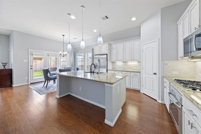 Sunlit kitchen featuring a gleaming granite island, sleek stainless-steel appliances, crisp white cabinetry, and a charming breakfast nook with inviting views of the backyard. | Image 8