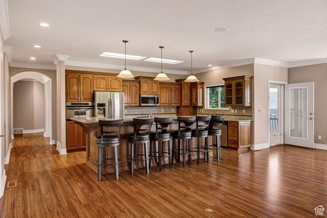 Kitchen with appliances with stainless steel finishes, arched walkways, brown cabinets, a kitchen bar, and recessed lighting | Image 7