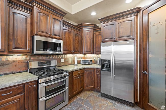 Kitchen featuring appliances with stainless steel finishes, stone tile flooring, tasteful backsplash, recessed lighting, and light stone countertops | Image 32