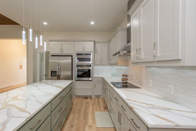 Kitchen featuring wall chimney exhaust hood, light wood-type flooring, decorative light fixtures, light stone counters, and stainless steel appliances | Image 9