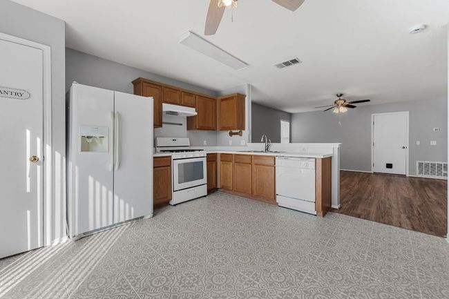 Kitchen with ceiling fan, white appliances, a peninsula, brown cabinetry, tile floor, and light countertops | Image 11