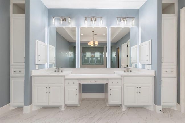 This luxurious primary bath features dual vanities, a dedicated makeup station, and dramatic backlit mirrors, all wrapped in soothing blue tones and polished with gleaming marble-look tile underfoot. | Image 22