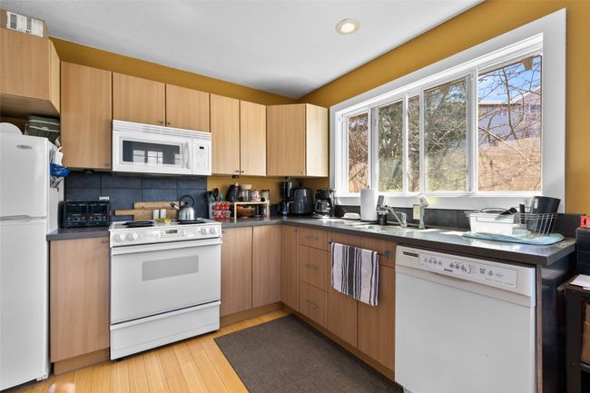 Kitchen with backsplash, dark countertops, a sink, white appliances, and light wood-style floors | Image 33