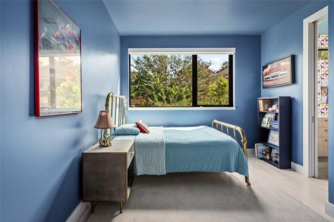 This cheerful secondary bedroom is wrapped in a bold blue hue by Farrow & Ball that brings playful energy and warmth. A large window fills the space with natural light and tree-filled views. The Jack & Jill bath just beyond offers added convenience and privacy. | Image 22
