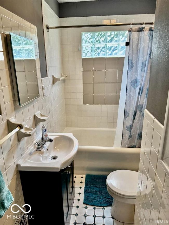 full bathroom with tile walls, shower / bathtub combination with curtain, vanity, and plenty of natural light | Image 29