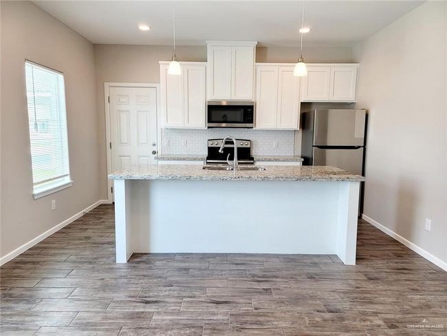 Kitchen with white cabinets, a kitchen island with sink, stainless steel appliances, a sink, and backsplash | Image 4