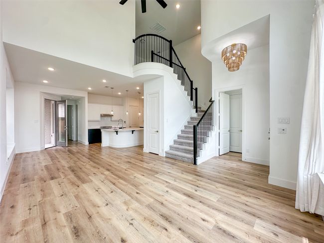 Unfurnished living room featuring stairway, a high ceiling, ceiling fan, light wood-type flooring, and recessed lighting | Image 4