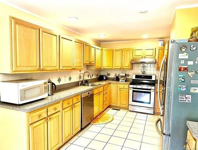 Kitchen with a sink, under cabinet range hood, light tile patterned floors, backsplash, and appliances with stainless steel finishes | Image 5