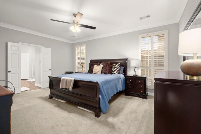 Primary bedroom offers plush carpet, ceiling fan, shutters, neutral paint and crown molding. | Image 19