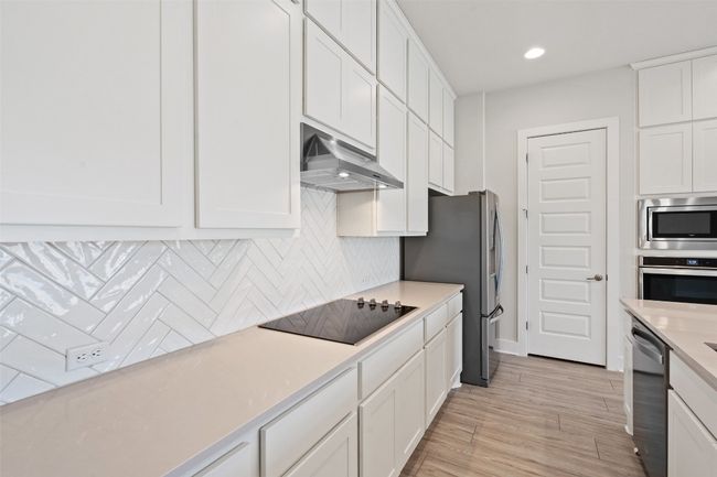Kitchen with white cabinetry, decorative backsplash, light countertops, light wood-style floors, and appliances with stainless steel finishes | Image 11