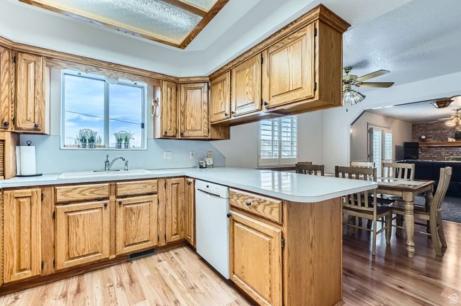 Kitchen with white dishwasher, a peninsula, a ceiling fan, light countertops, and light wood-style flooring | Image 5