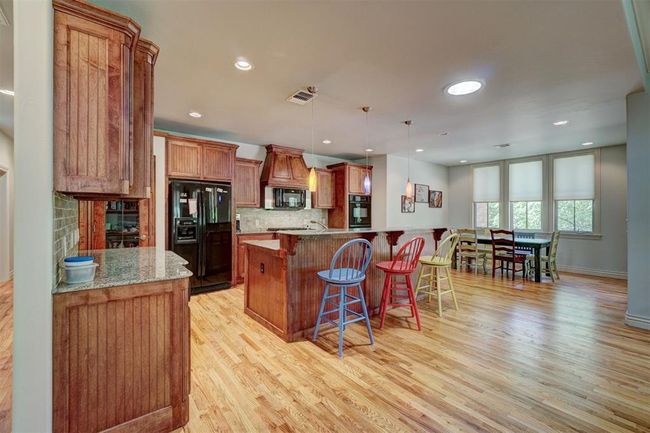 Kitchen with black appliances, a breakfast bar, light wood finished floors, backsplash, and visible vents | Image 10