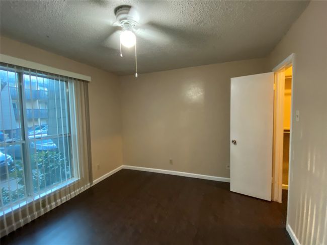 Empty room with a textured ceiling, baseboards, dark wood finished floors, a wealth of natural light, and a ceiling fan | Image 12