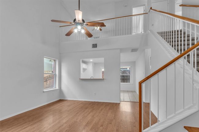 Unfurnished living room with ceiling fan, stairway, wood finished floors, and a high ceiling | Image 8
