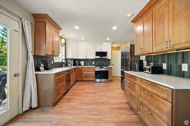 Kitchen with appliances with stainless steel finishes, tasteful backsplash, light wood finished floors, recessed lighting, and light countertops | Image 9