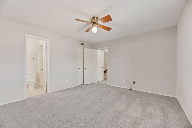 Unfurnished bedroom featuring light colored carpet, connected bathroom, a textured ceiling, and ceiling fan | Image 12