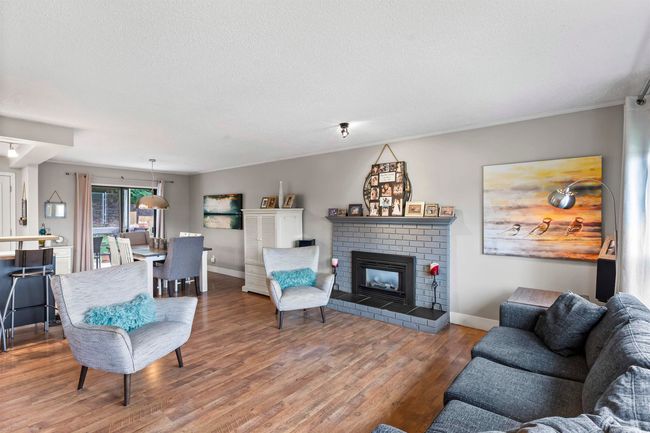 Living area with a textured ceiling, wood finished floors, baseboards, and a brick fireplace | Image 6
