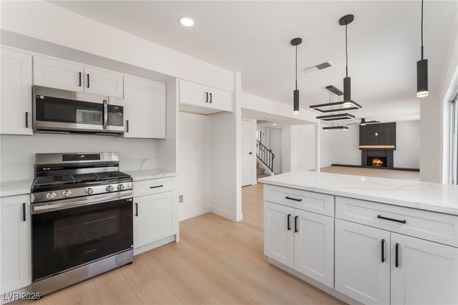 Kitchen with stainless steel appliances, white cabinets, a warm lit fireplace, light wood finished floors, and light stone counters | Image 17