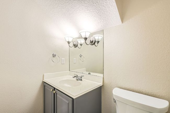 Half bathroom featuring a textured wall, vanity, a notable chandelier, and toilet | Image 21