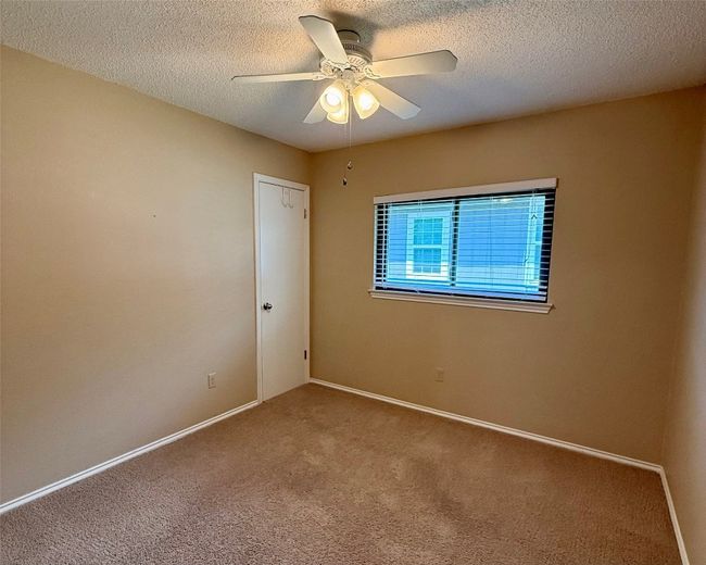 Carpeted empty room with a ceiling fan, a textured ceiling, and baseboards | Image 12
