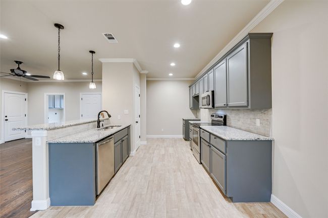 Kitchen with appliances with stainless steel finishes, gray cabinets, a sink, a ceiling fan, and light stone countertops | Image 8