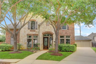 THIS ELEGANT TWO-STORY HOME FEATURES A STONE AND BRICK EXTERIOR WITH MATURE TREES AND A WELCOMING FRONT DOOR. | Image 1