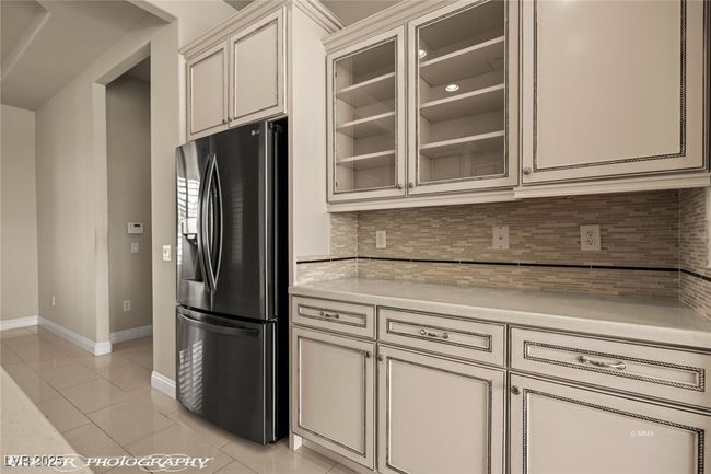 Kitchen featuring refrigerator with ice dispenser, light tile patterned flooring, cream cabinets, baseboards, and backsplash | Image 18
