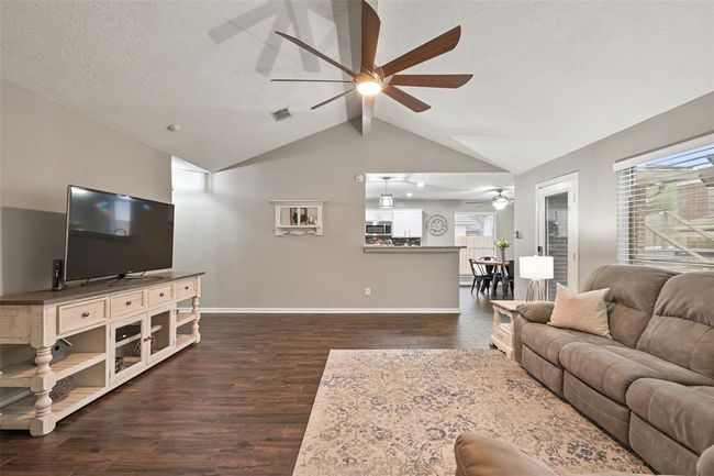 Proceed to the spacious family room with soaring vaulted ceilings, a sleek modern ceiling fan, and wood-look tile flooring. Open sightlines to the kitchen and breakfast area make this space ideal for entertaining and everyday living. | Image 8