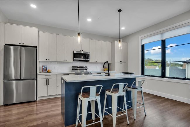 Kitchen with appliances with stainless steel finishes, a sink, a center island with sink, backsplash, and a kitchen bar | Image 9