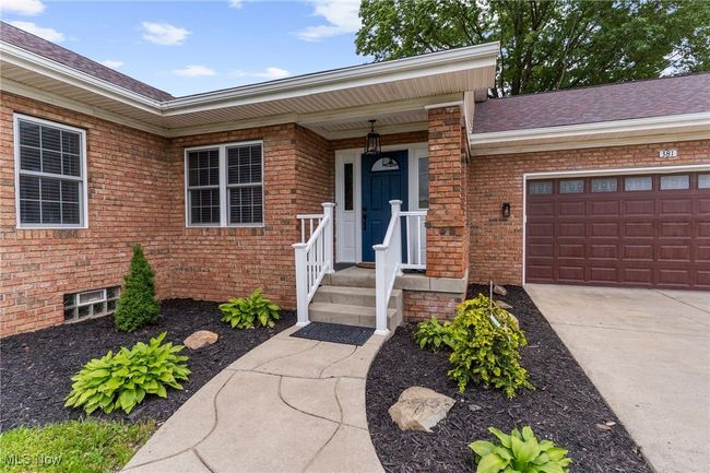 Doorway to property featuring brick siding, an attached garage, roof with shingles, and driveway | Image 5