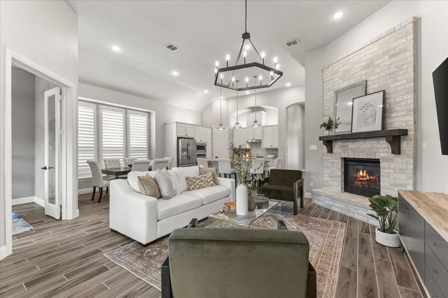 Living room with wood tiled floors, recessed lighting, a brick fireplace, a chandelier, and high vaulted ceiling | Image 11