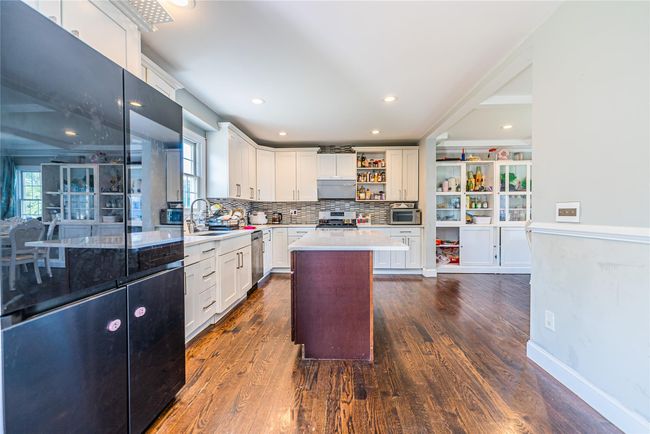 Kitchen with stainless steel appliances, open shelves, under cabinet range hood, decorative backsplash, and dark wood-type flooring | Image 17