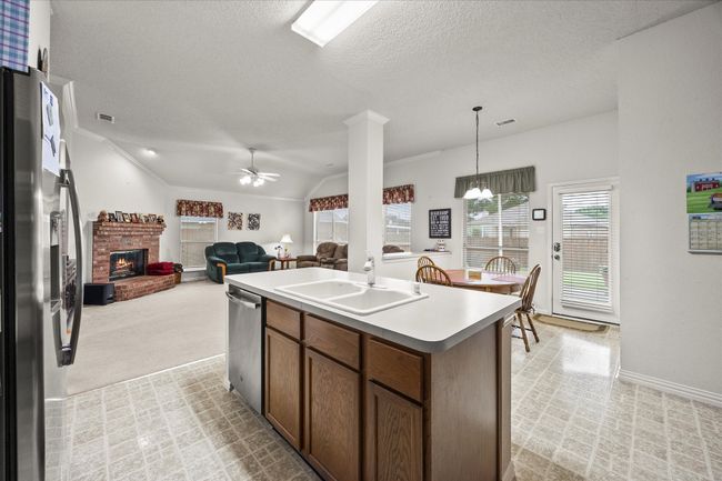 Kitchen featuring appliances with stainless steel finishes, a brick fireplace, ceiling fan, a kitchen island with sink, and a textured ceiling | Image 19