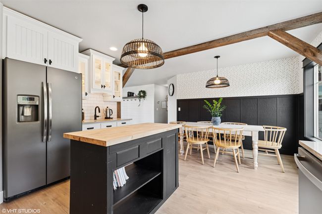 Kitchen featuring stainless steel fridge with ice dispenser, open shelves, white cabinets, decorative light fixtures, and wooden counters | Image 14