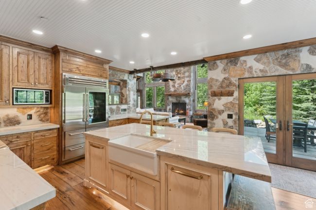 Kitchen with built in appliances, a fireplace, french doors, light wood finished floors, and light stone countertops | Image 11