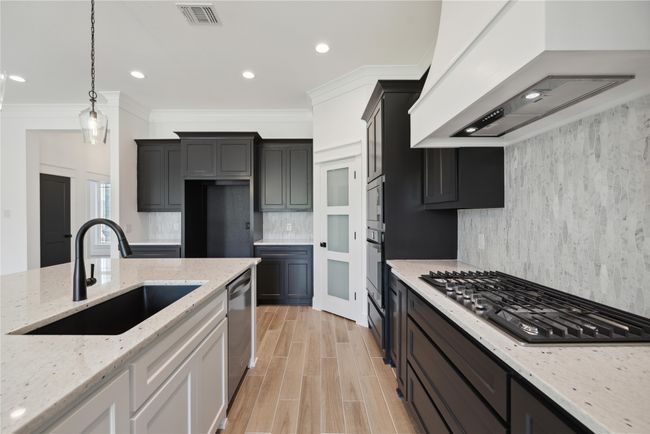 Kitchen with premium range hood, appliances with stainless steel finishes, white cabinetry, sink, and light stone counters | Image 17