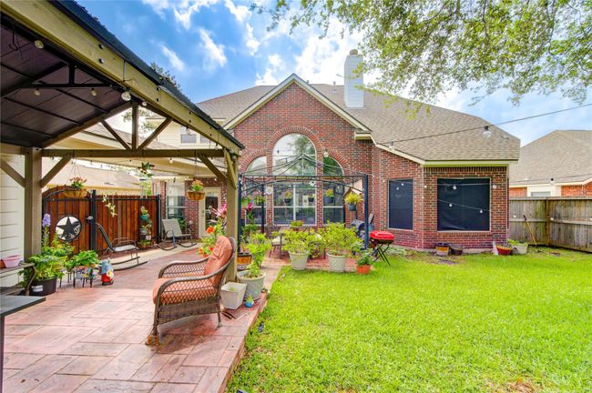 Charming backyard with a brick exterior, featuring a covered patio area perfect for relaxation. The lawn is well-maintained, and there are potted plants adding a touch of greenery. Ideal for outdoor gatherings and enjoying sunny days. | Image 4