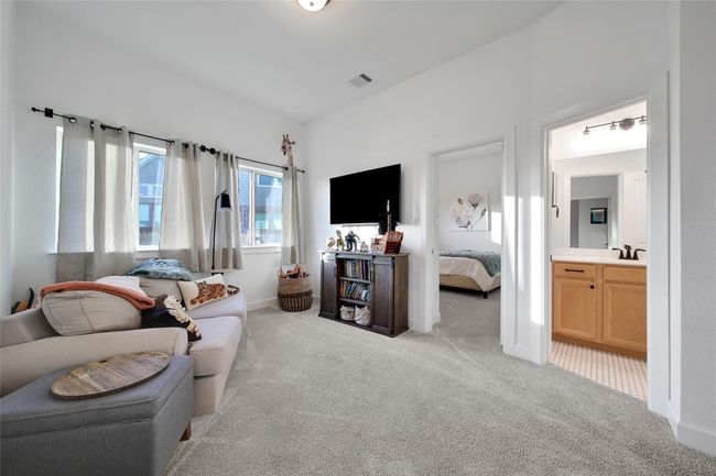 A cozy, carpeted living area with natural light from large windows, featuring a comfortable sofa, wall-mounted TV, and access to a bedroom and bathroom. | Image 34