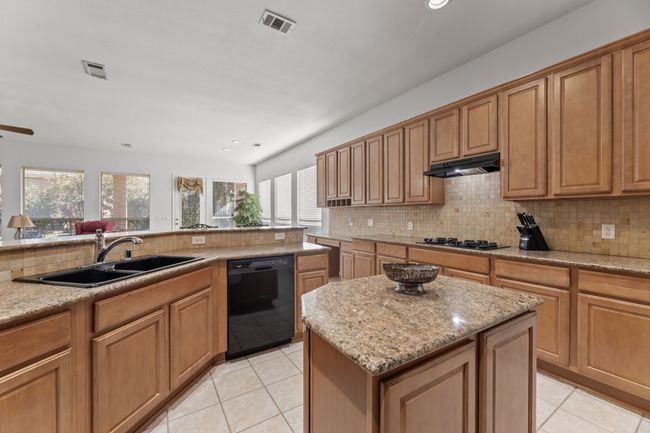 Kitchen featuring sink, a center island, tasteful backsplash, black appliances, and light stone countertops | Image 17