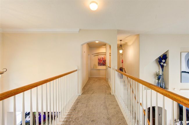 Bright hallway with neutral walls and carpet, featuring a wooden railing. An archway leads to another area, with decorative lighting and art adding a welcoming touch. Perfect for adding personal decor. | Image 25