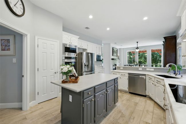 Kitchen with appliances with stainless steel finishes, white cabinets, cermainc tile wood-type flooring, light natural stone countertops, and recessed lighting | Image 12