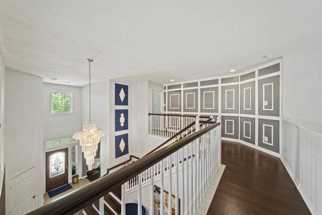 A striking view from the upstairs landing showcases custom accent wall panels and a sparkling crystal chandelier above the elegant foyer below. | Image 30
