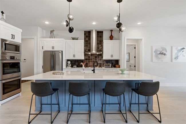 Kitchen featuring stainless steel appliances, white cabinetry, wall chimney exhaust hood, light wood-type flooring, and backsplash | Image 12