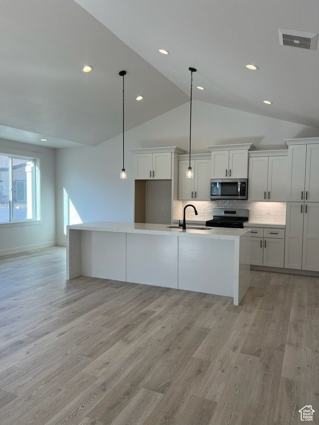 Kitchen featuring appliances with stainless steel finishes, a sink, lofted ceiling, recessed lighting, and light wood-type flooring | Image 5