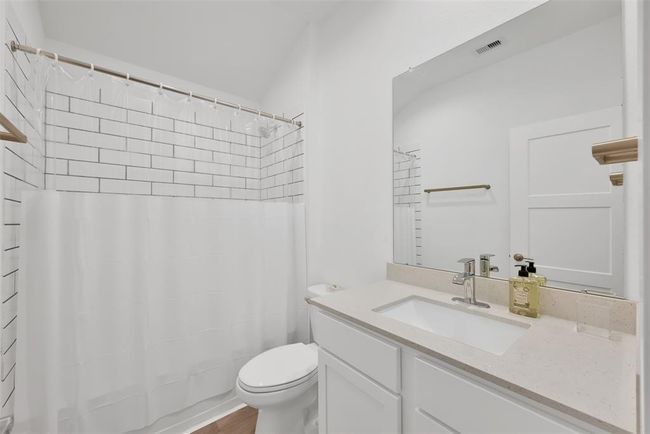 This bathroom features a clean, modern design with white subway tiles in the shower, a sleek vanity with a quartz countertop, and a large mirror. | Image 16