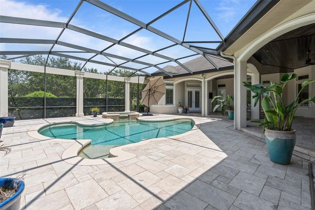 The beautifully designed screened-in pool area features a spa, sun shelf, and expansive travertine deck—perfect for lounging, entertaining, and enjoying the Florida lifestyle in total comfort. | Image 28