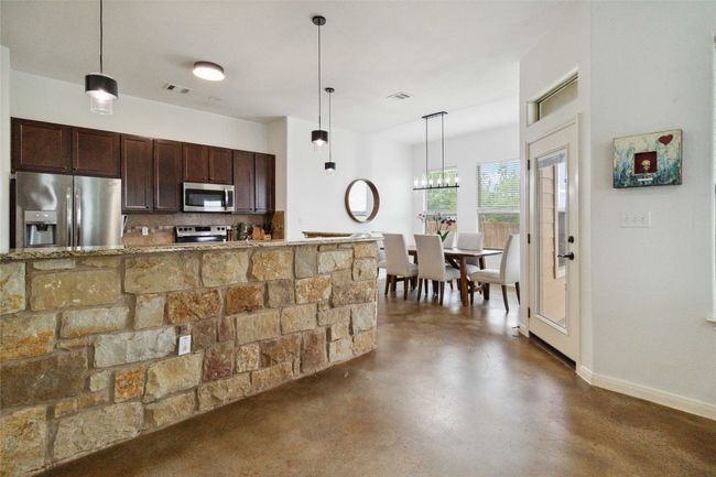 Kitchen featuring appliances with stainless steel finishes, finished concrete floors, dark brown cabinets, decorative backsplash, and decorative light fixtures | Image 9
