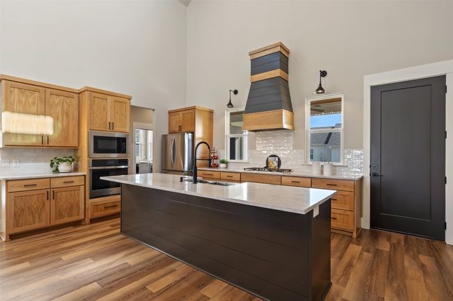 Kitchen featuring stainless steel appliances, a sink, a high ceiling, custom range hood, and decorative backsplash | Image 10
