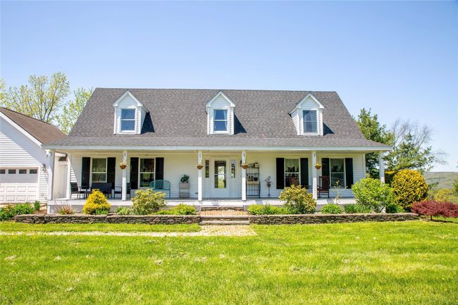 Cape cod-style house featuring covered porch, a front yard, a shingled roof, and a garage | Image 5